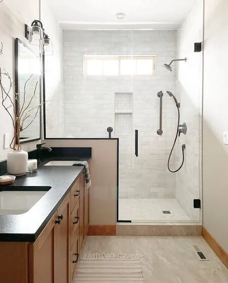 Bathroom with a walk-in shower, glass door, and a black vanity with a sink and mirror, natural light from a small window.