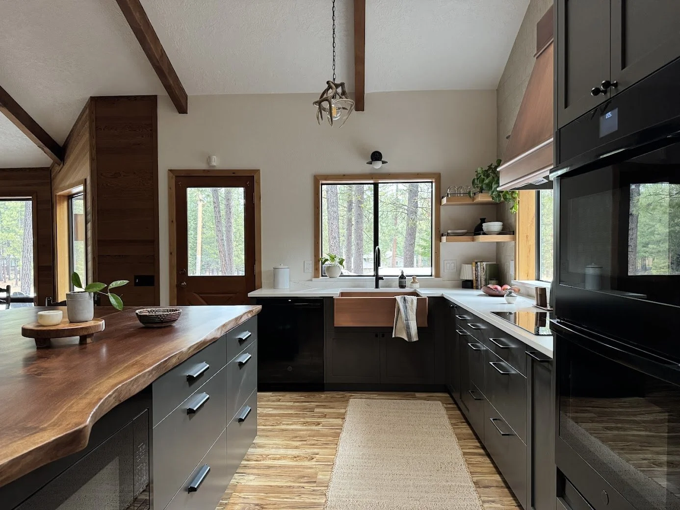 Kitchen with black cabinets, wooden countertops, and large windows with a view of trees outside.