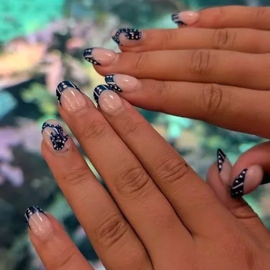 Close-up of hands showing manicured nails with French tips and black nail art with white polka dots and curved lines.