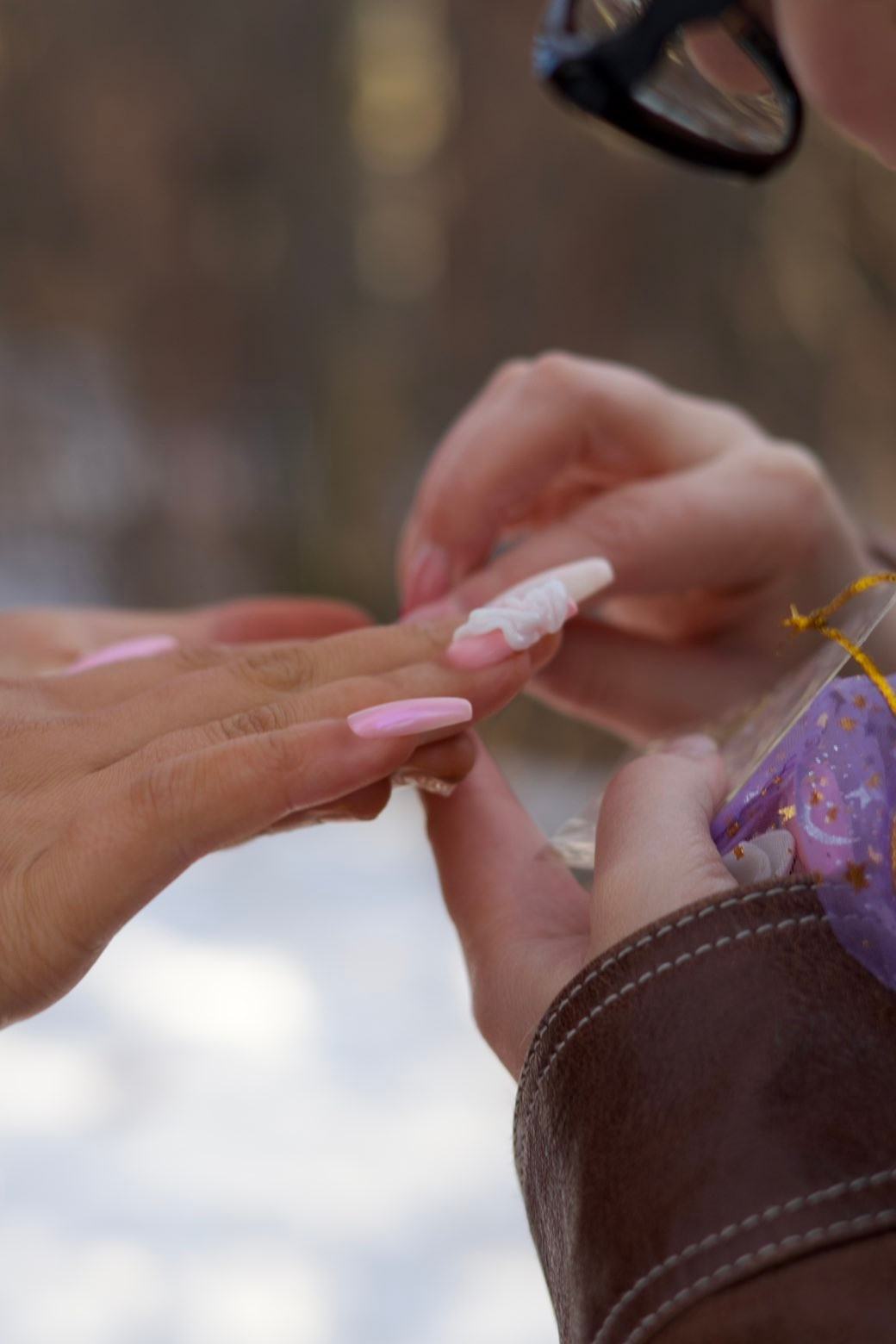 Someone is applying nail polish to another person's fingernails outdoors.