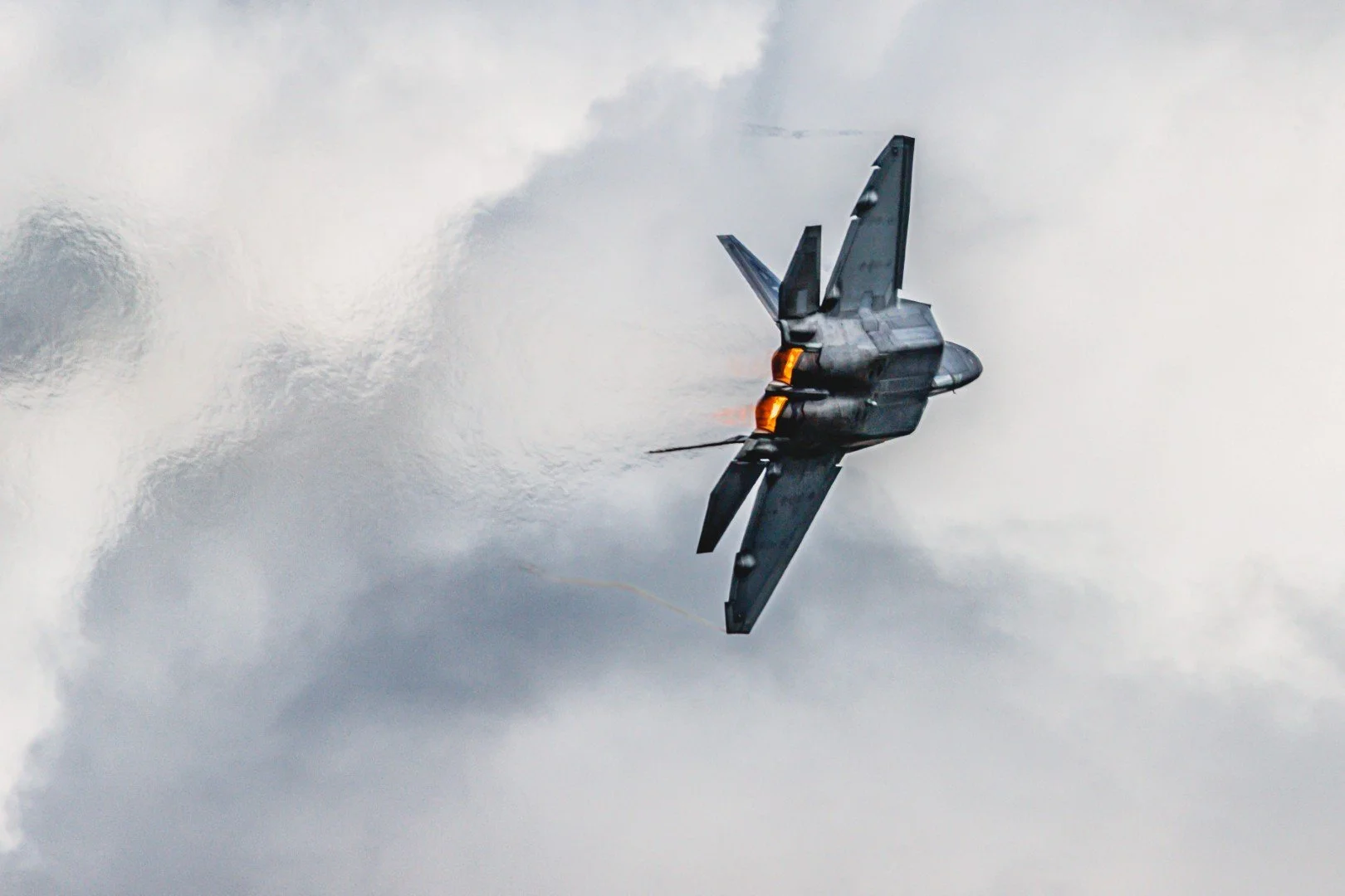 A fighter jet flying through cloudy skies with afterburners lit.