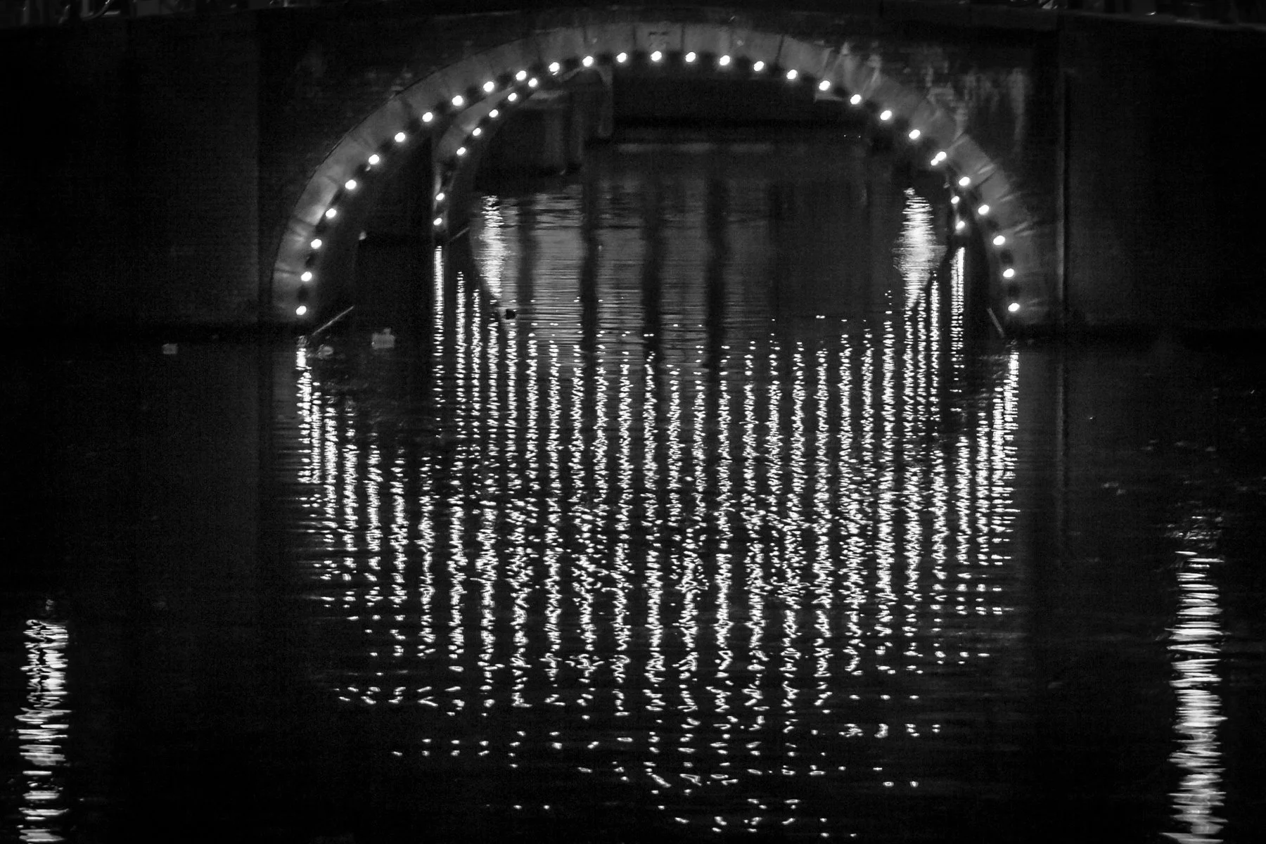 A dark bridge with lights reflecting on the water below.