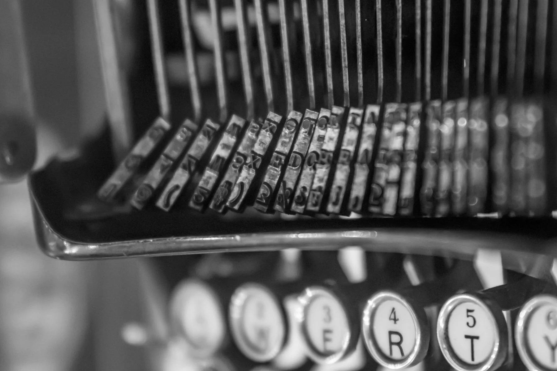 Close-up of vintage typewriter keys showing a row of metal letter keys with letters and symbols, captured in a black and white photograph.