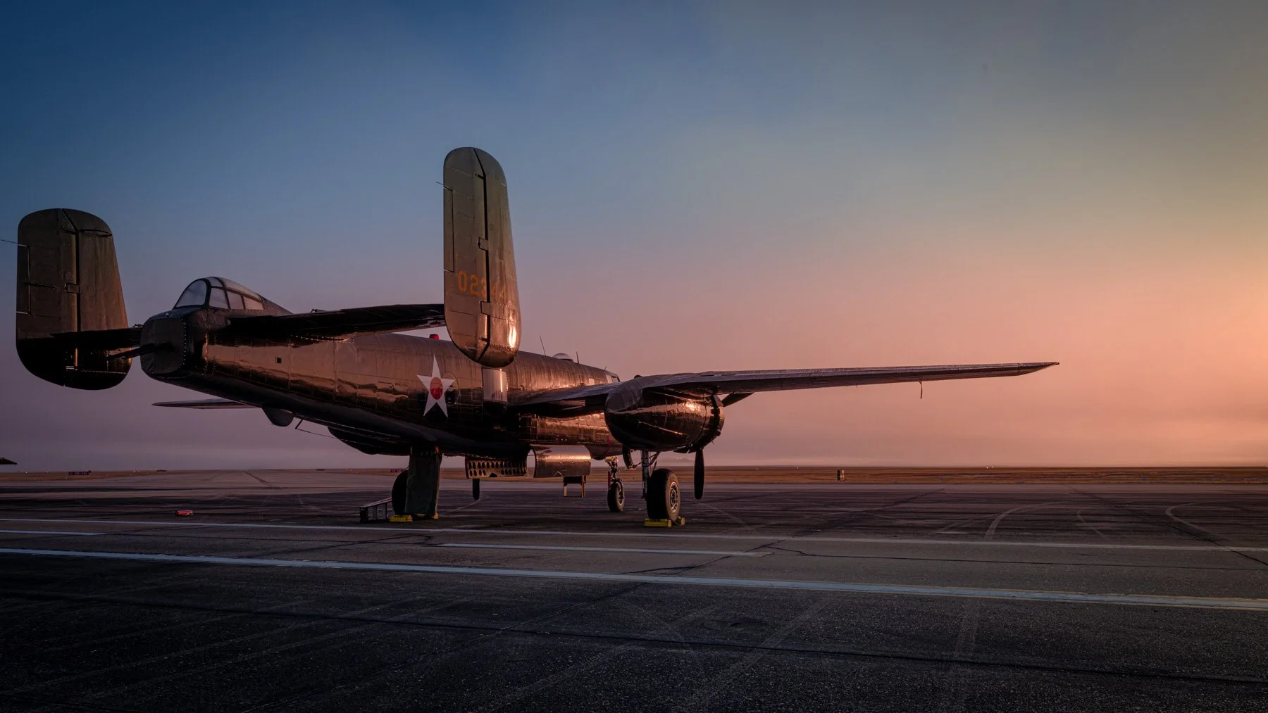 A vintage military jet aircraft parked on an airfield at sunrise with a clear sky.