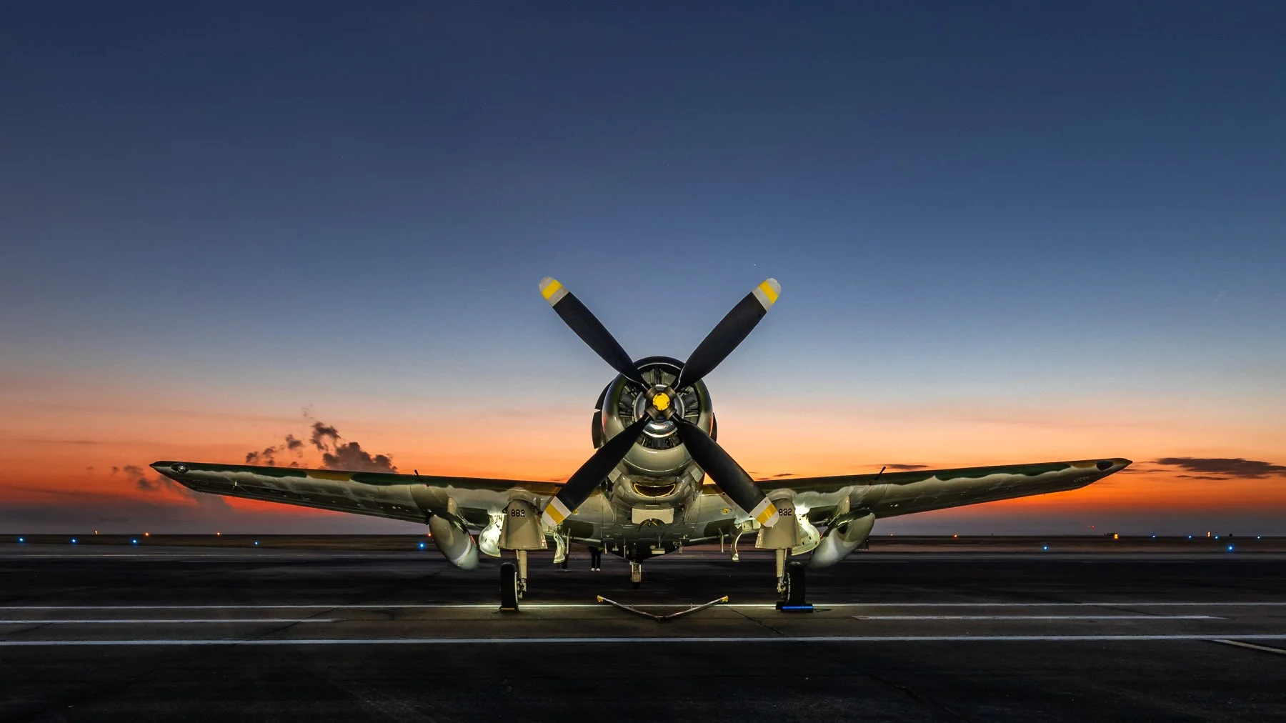 Front view of a military fighter jet aircraft at sunrise, with a propeller and wings visible, and the sky transitioning from orange to dark blue.