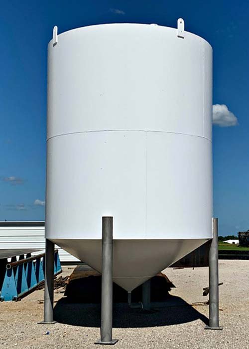 Large white storage tank elevated on metal supports outdoors under a blue sky.