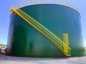 Large green industrial storage tank with yellow staircase and railing.