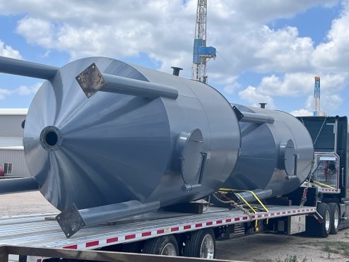 Large industrial tank on a flatbed truck at an outdoor construction site with cranes in the background.