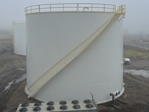 Large white industrial storage tank with an external staircase and a safety railing on top.