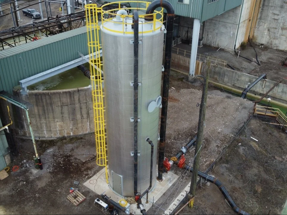 Industrial water tank with yellow safety railing and black pipes in an industrial yard.