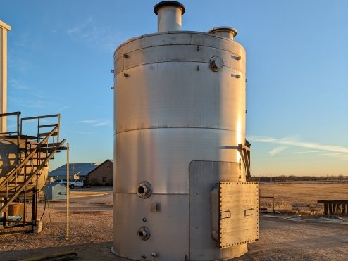 Large vertical metallic industrial storage tank outdoors at sunset.