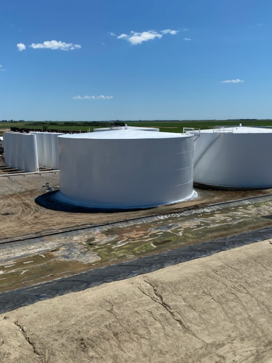 Large white industrial storage tanks on a rooftop under a blue sky with some clouds.