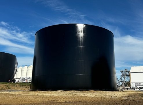 Large black cylindrical storage tank outdoors with a blue sky and clouds in the background.