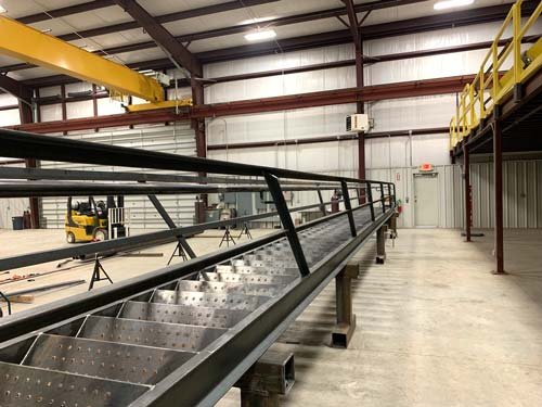 View of an industrial warehouse with a long metal conveyor belt and a yellow overhead crane.