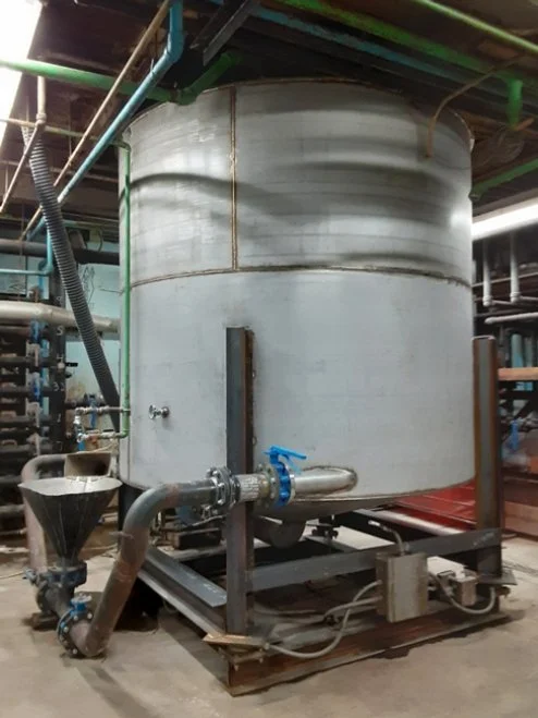 Large industrial stainless steel tank with pipes and valves in a factory or processing plant.
