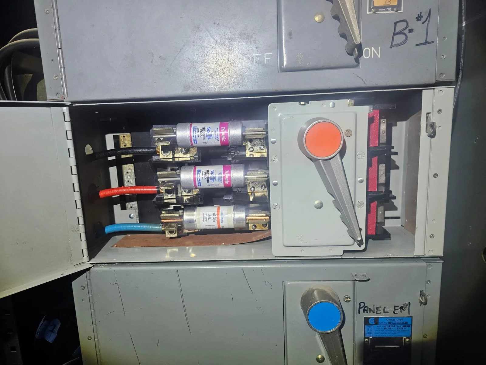 Open electrical panel with three relays and a red and blue cable connected, large gray handle on a switch inside the panel.