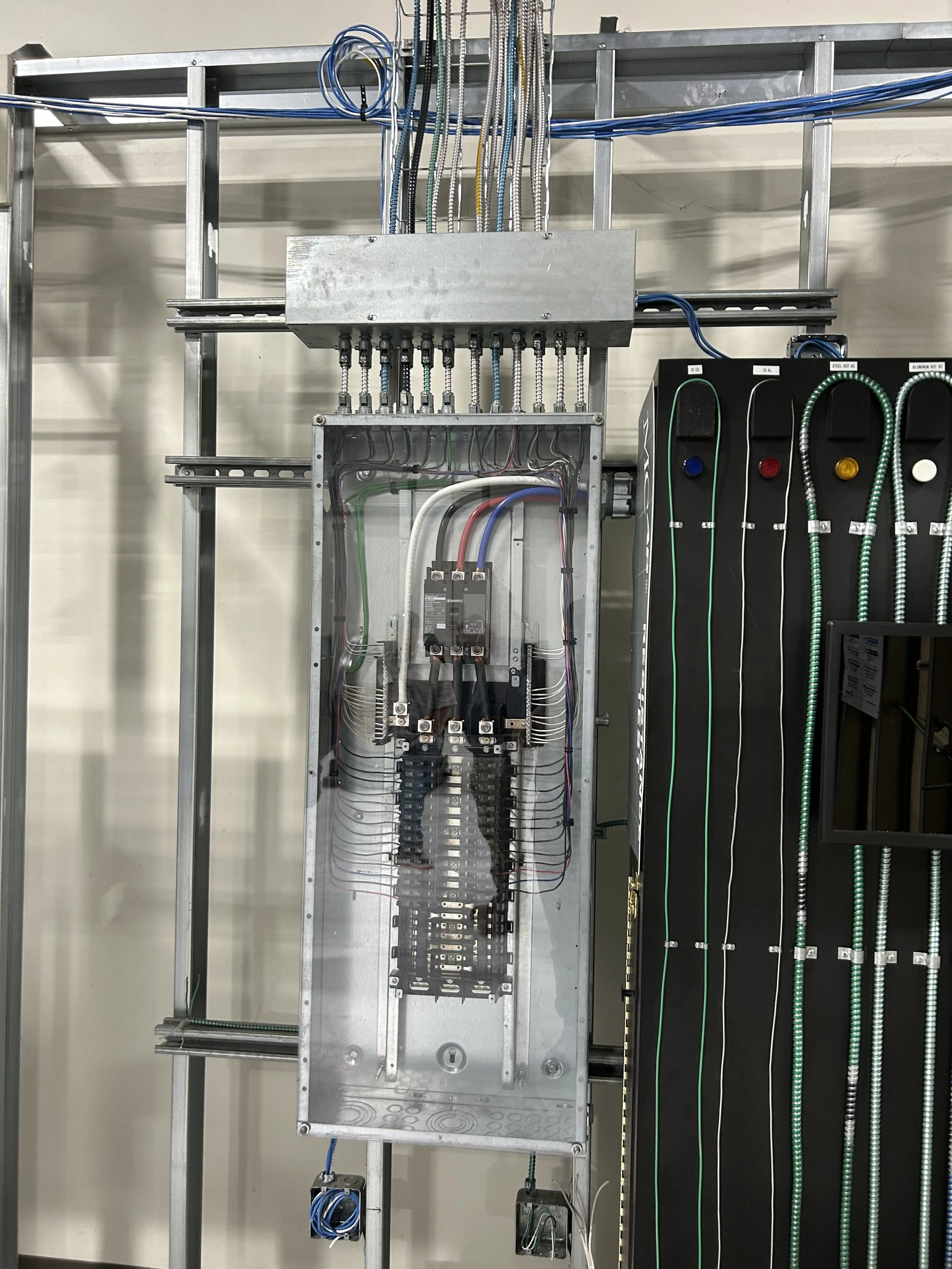 Close-up of an electrical panel with multiple colored wires connected to circuit breakers, mounted on a metallic frame with wiring conduits.