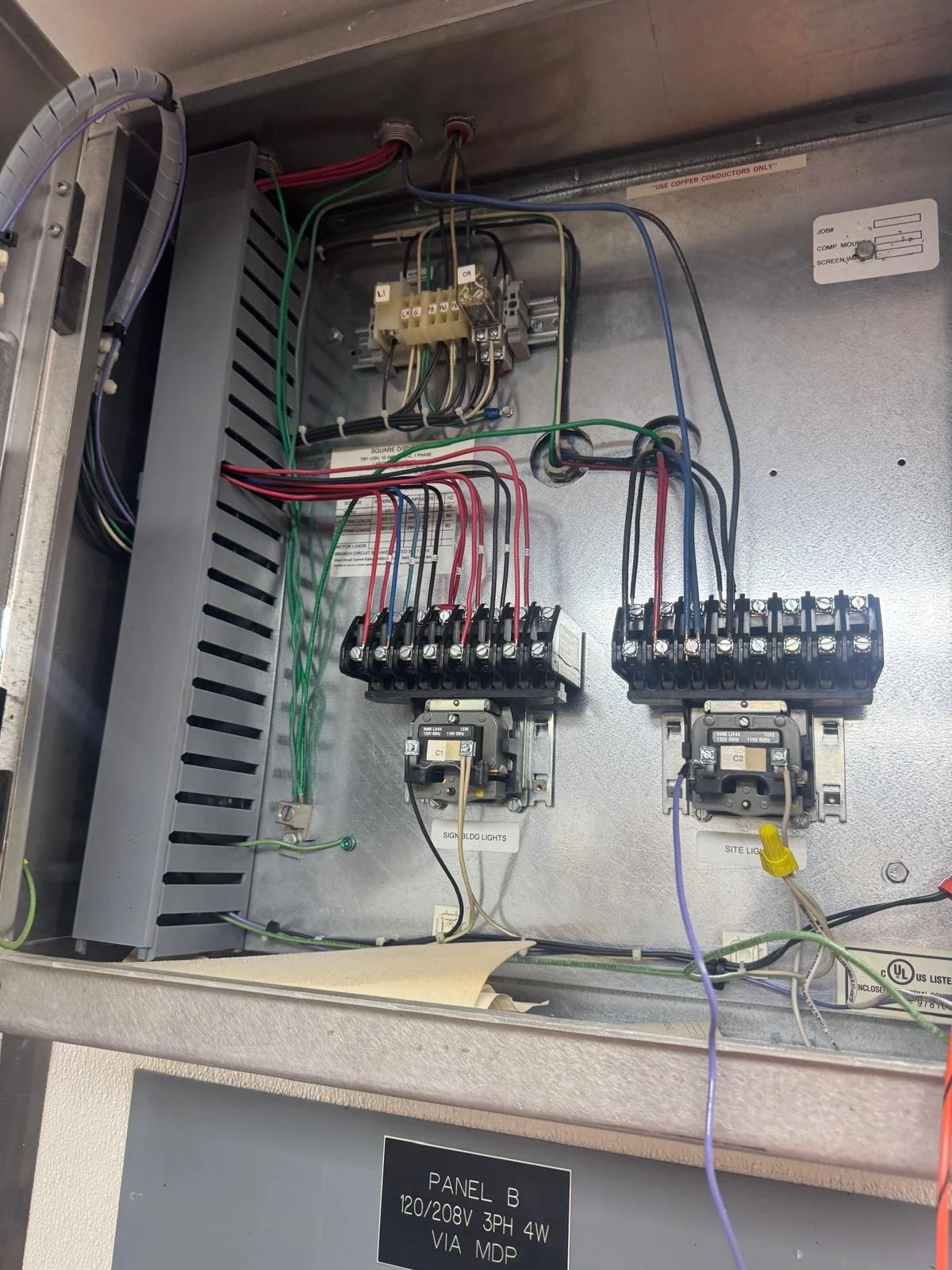 The image shows the inside of an electrical panel with connected wires, circuit breakers, and a relay. Labels are visible indicating circuit functions like 'SIGNAL LIGHTS' and 'SITE LIGHTS.'