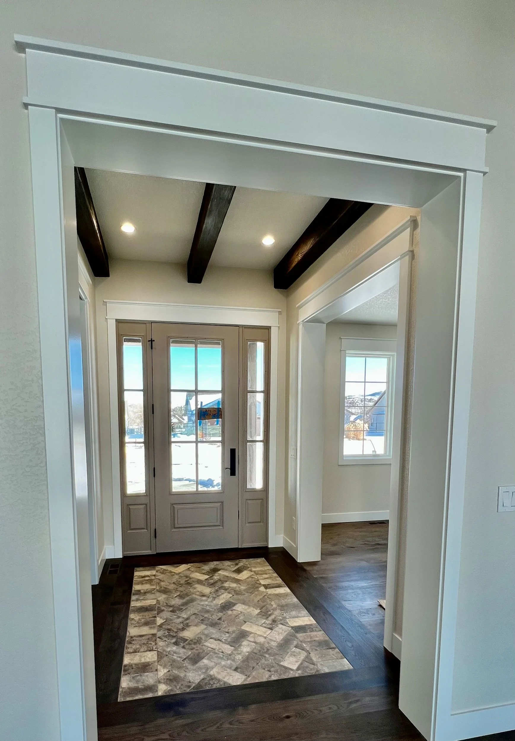Entryway with front door, side windows, wood beams on ceiling, hardwood floors, and patterned tile area.