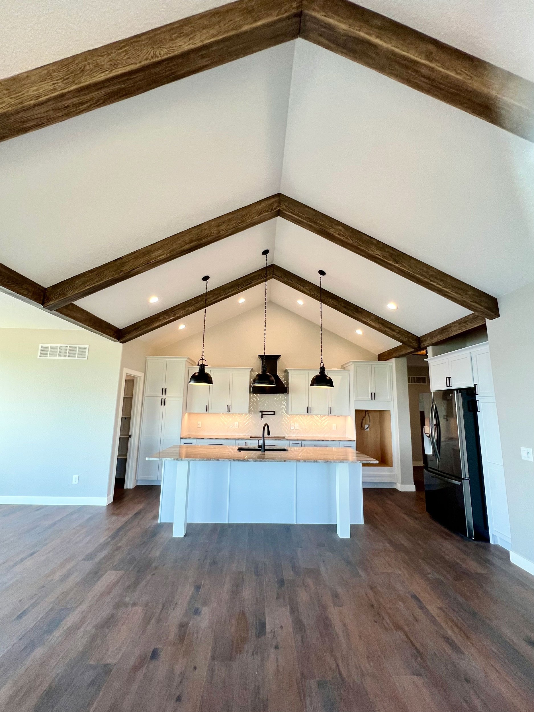 Modern open-concept kitchen with white cabinetry, a kitchen island with a wooden countertop, black pendant lighting, and a vaulted ceiling with wooden beams.