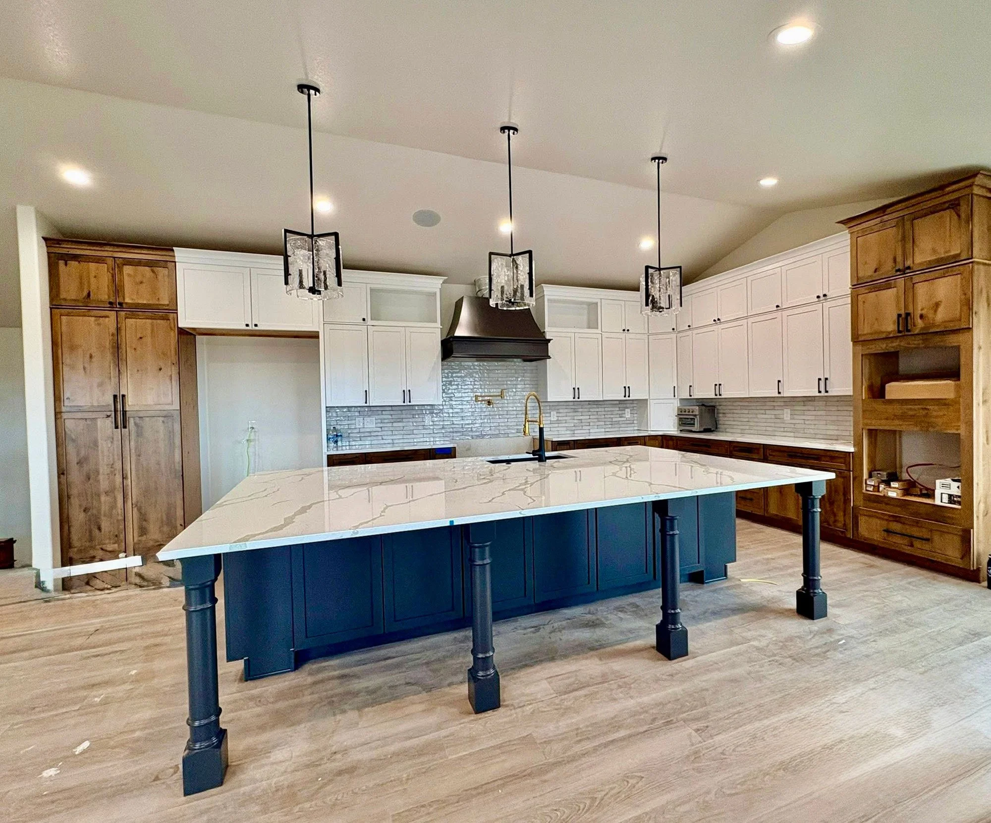 Modern kitchen with large island painted dark blue, white marble countertop, black pendant lights, white cabinets, and wooden accents.