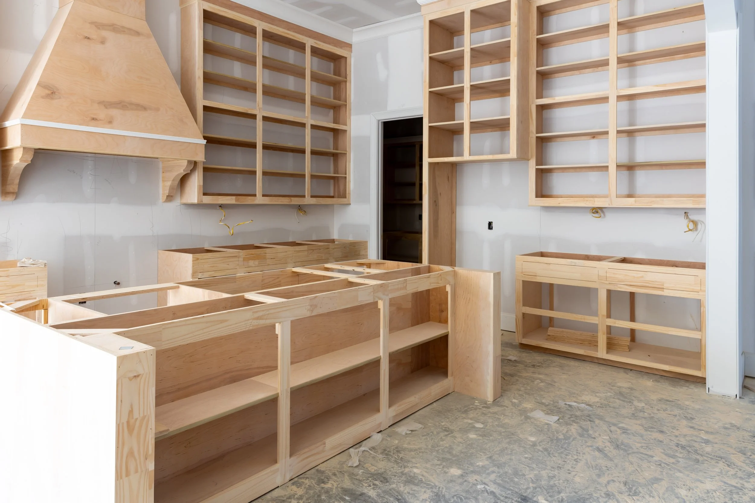 Empty wooden cabinets and shelving units inside a room under construction or renovation.