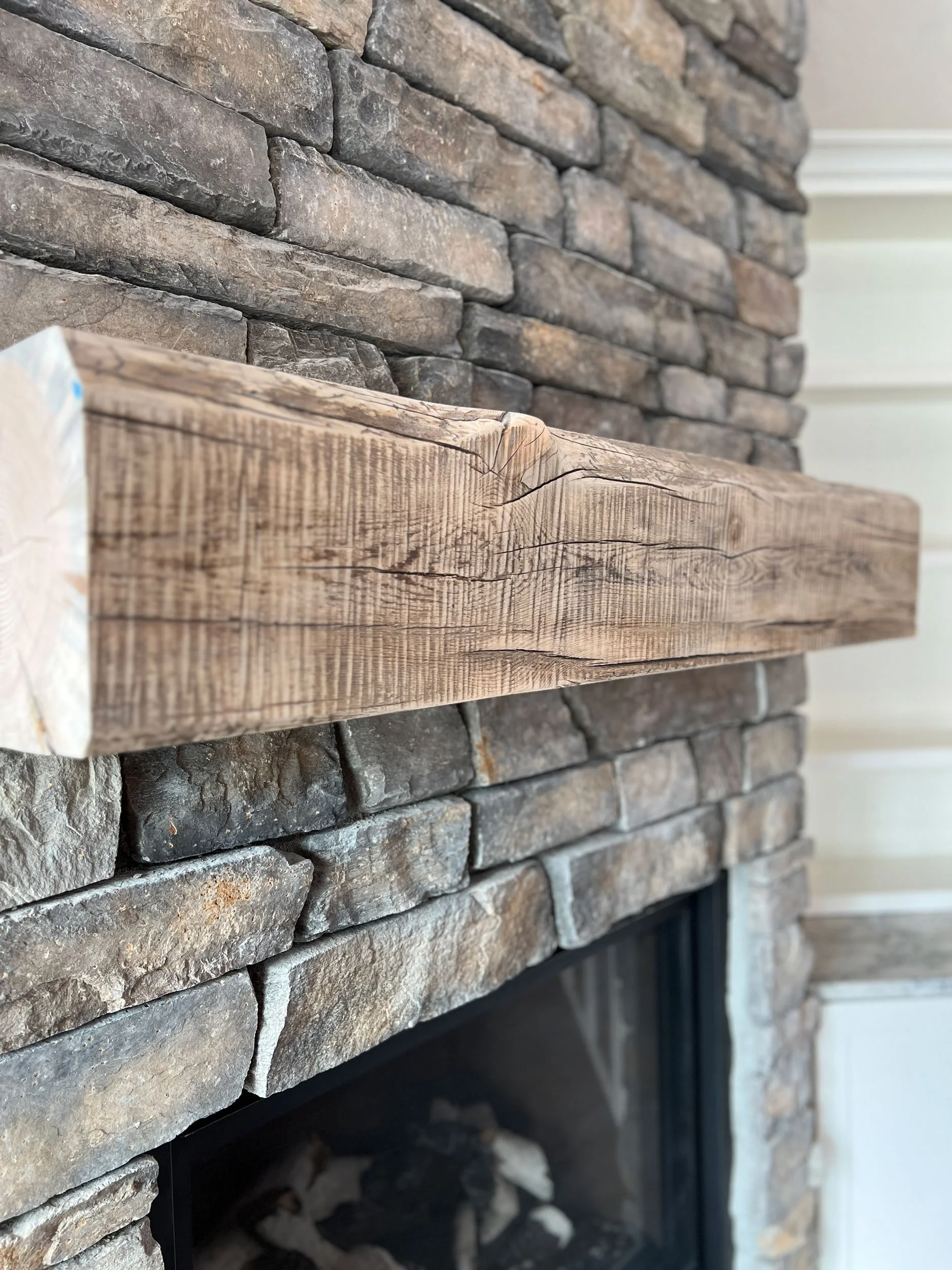 Close-up of a fireplace with stacked stone facade and a wooden mantel.