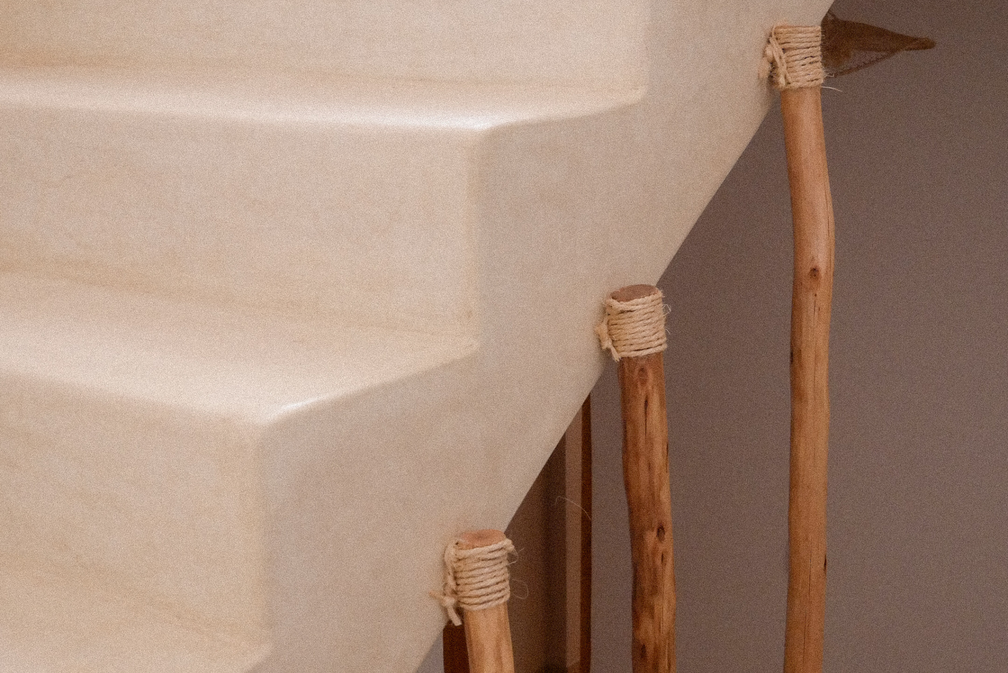 Close-up of a white ceramic bathtub or sink with wooden legs wrapped with rope, set against a light wall.