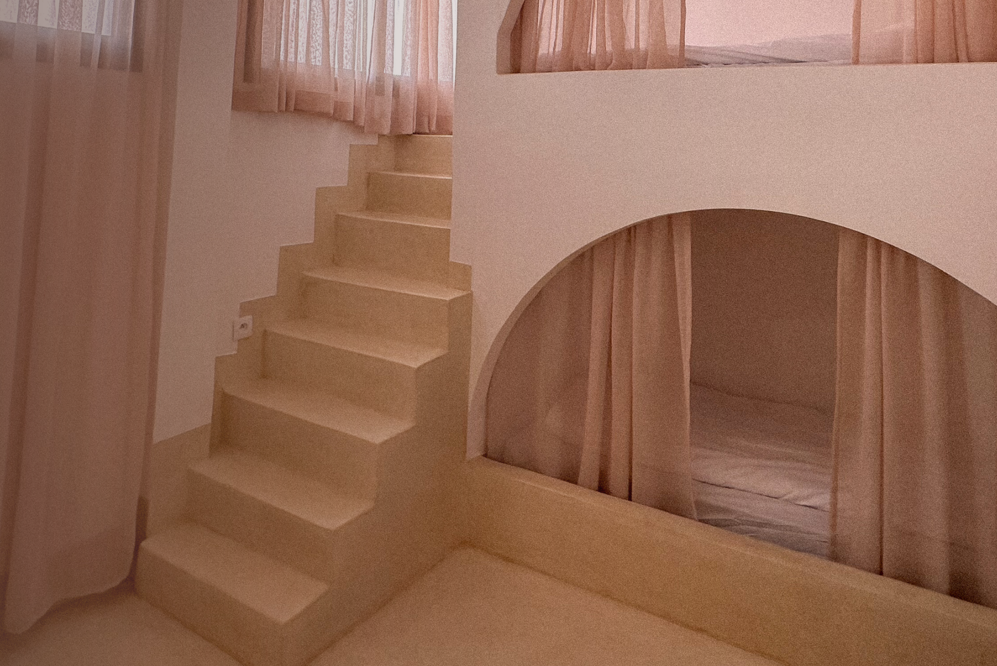 Unfinished light-colored wood staircase with a curved archway underneath, and pink curtains on windows in the background.