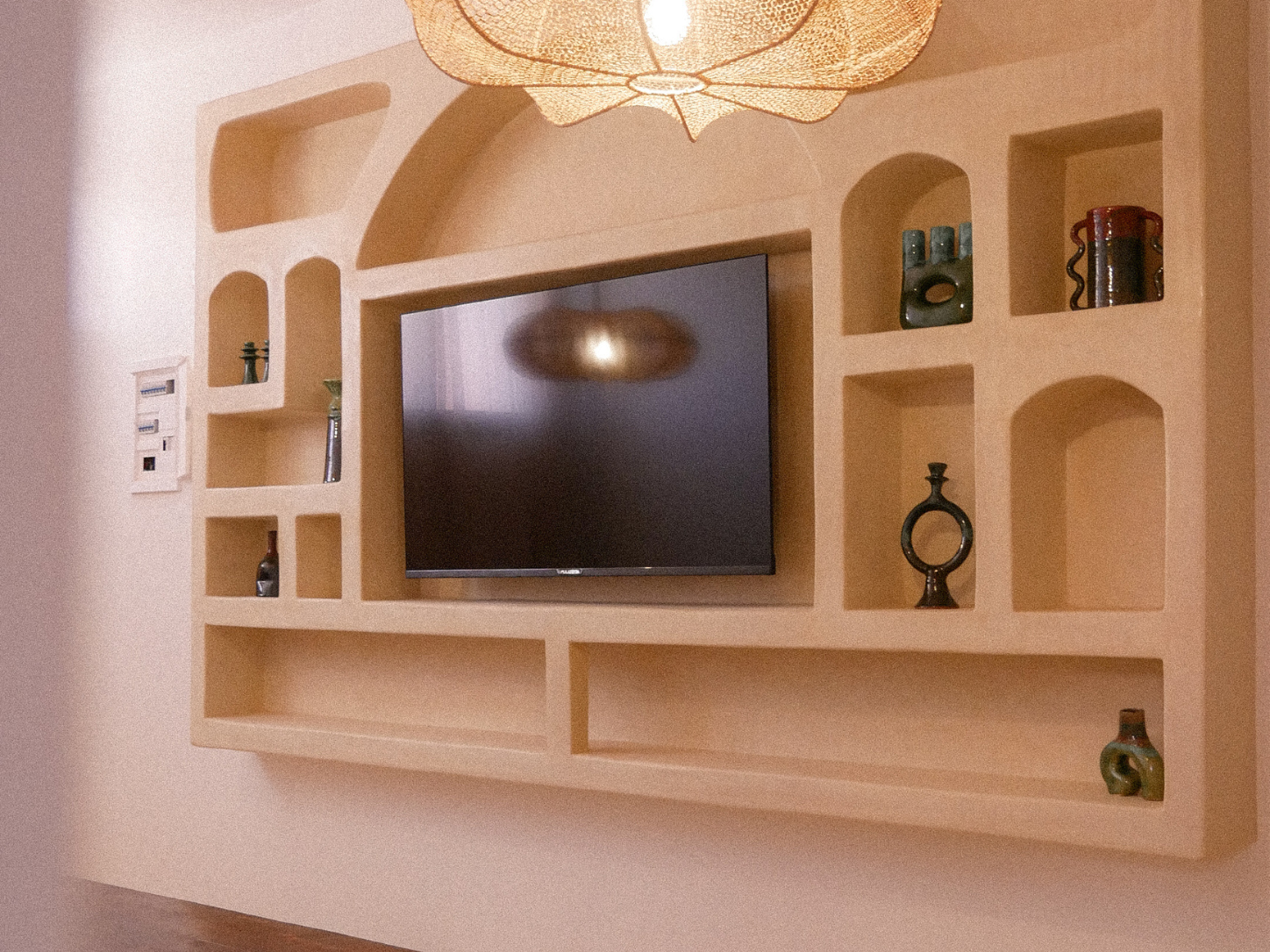 A wall-mounted entertainment center with a flat-screen TV and multiple decorative shelves containing various small art pieces and vases.