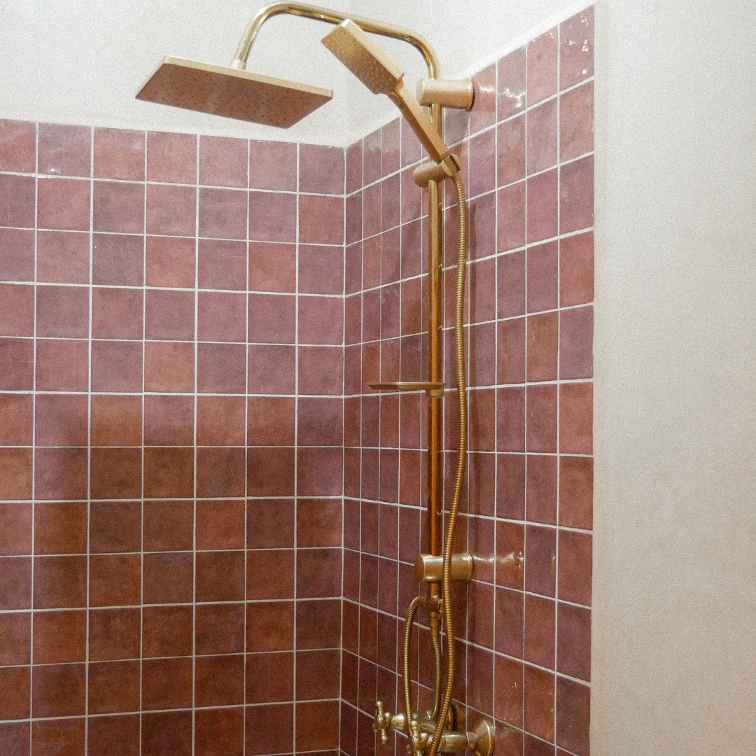 Shower with pink tiled wall and gold-colored shower fixtures, including a rainfall showerhead and handheld showerhead.