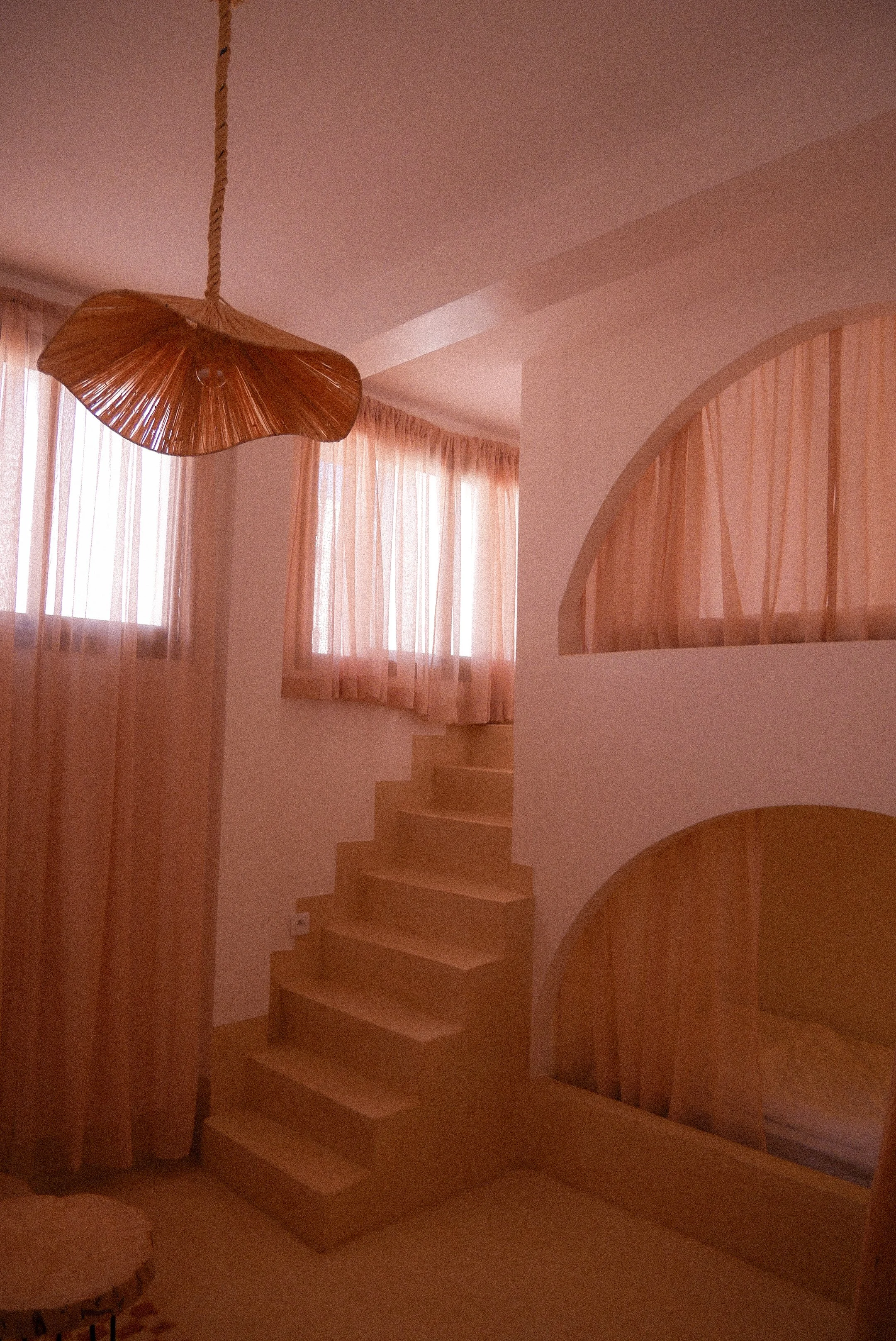 Interior view of a staircase and window with pink curtains, with a wooden hanging light fixture.