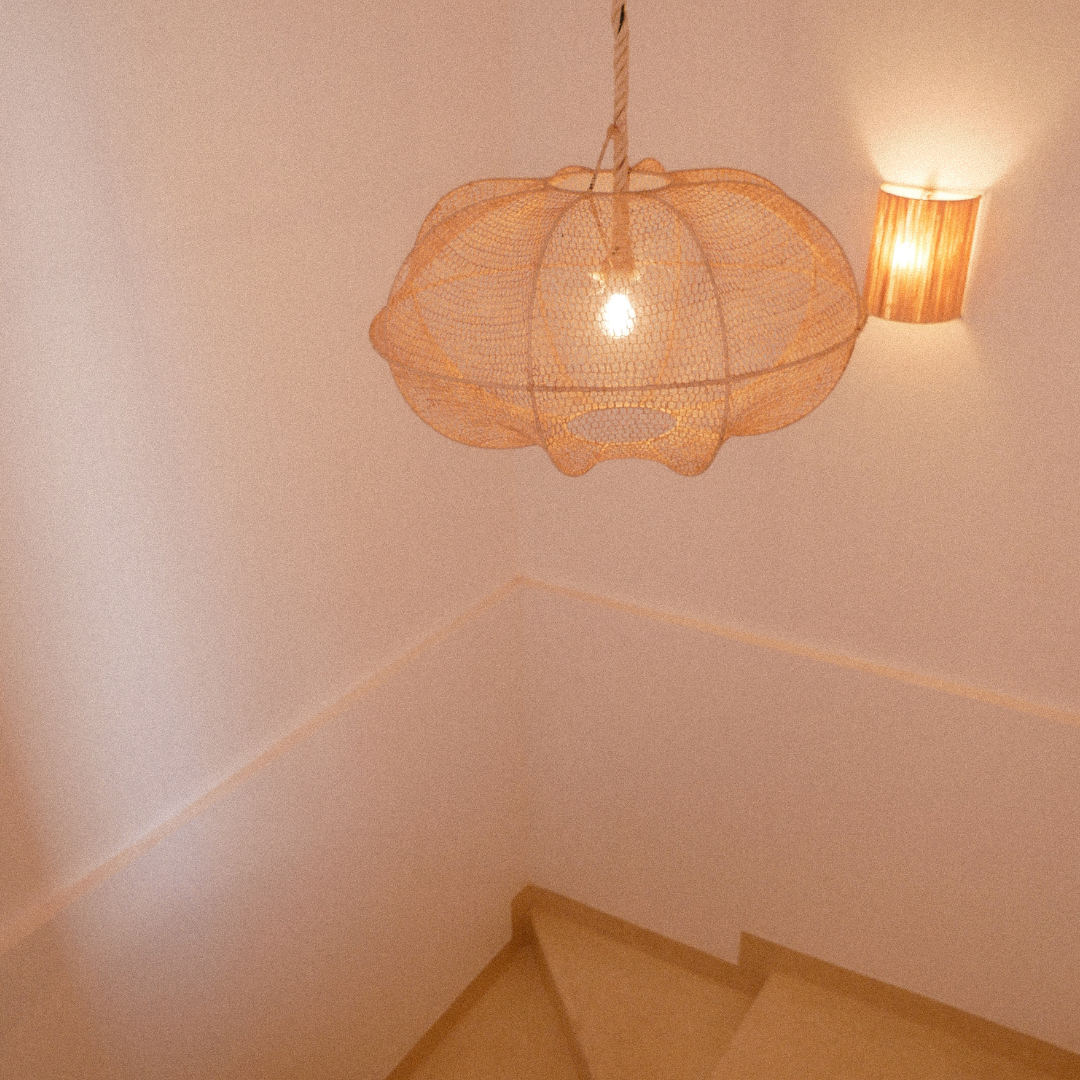 A stairwell with a hanging orange lampshade and a wall-mounted light fixture on a pink wall.