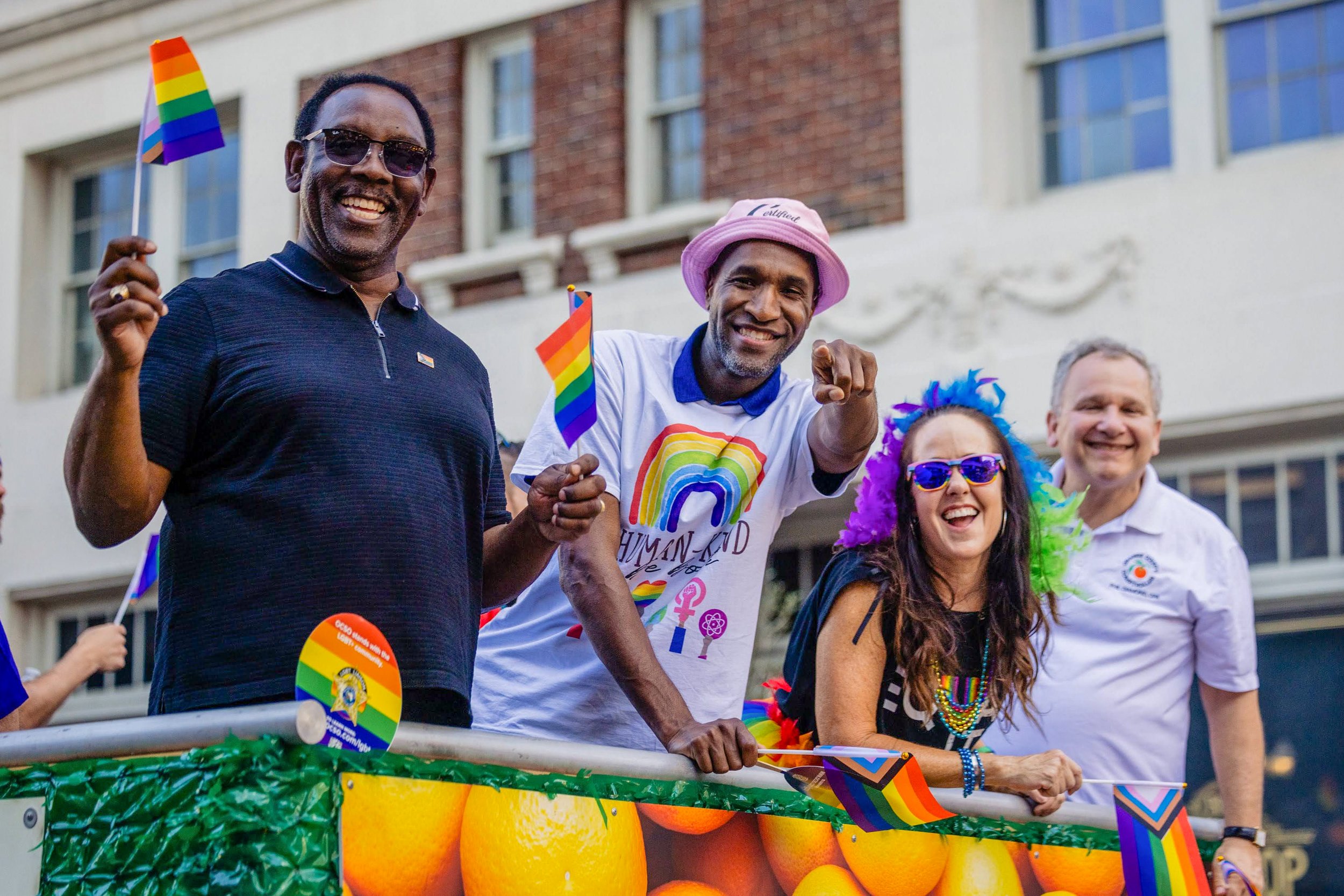 People celebrating at a pride parade, dressed in colorful clothing and accessories, holding rainbow flags and banners.