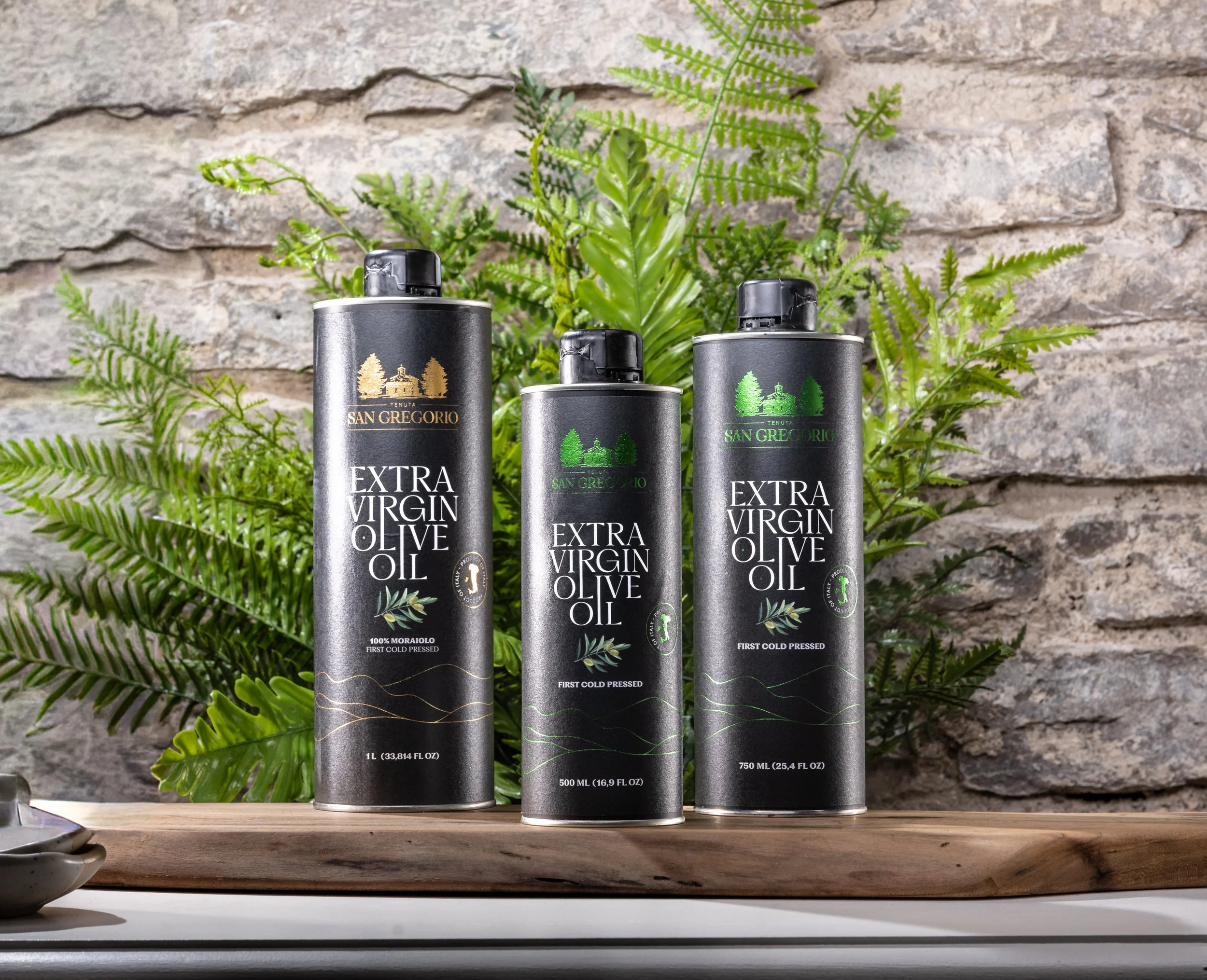 3 bottles of Sand Gregorio olive oil with plants and an exposed brick wall in the background