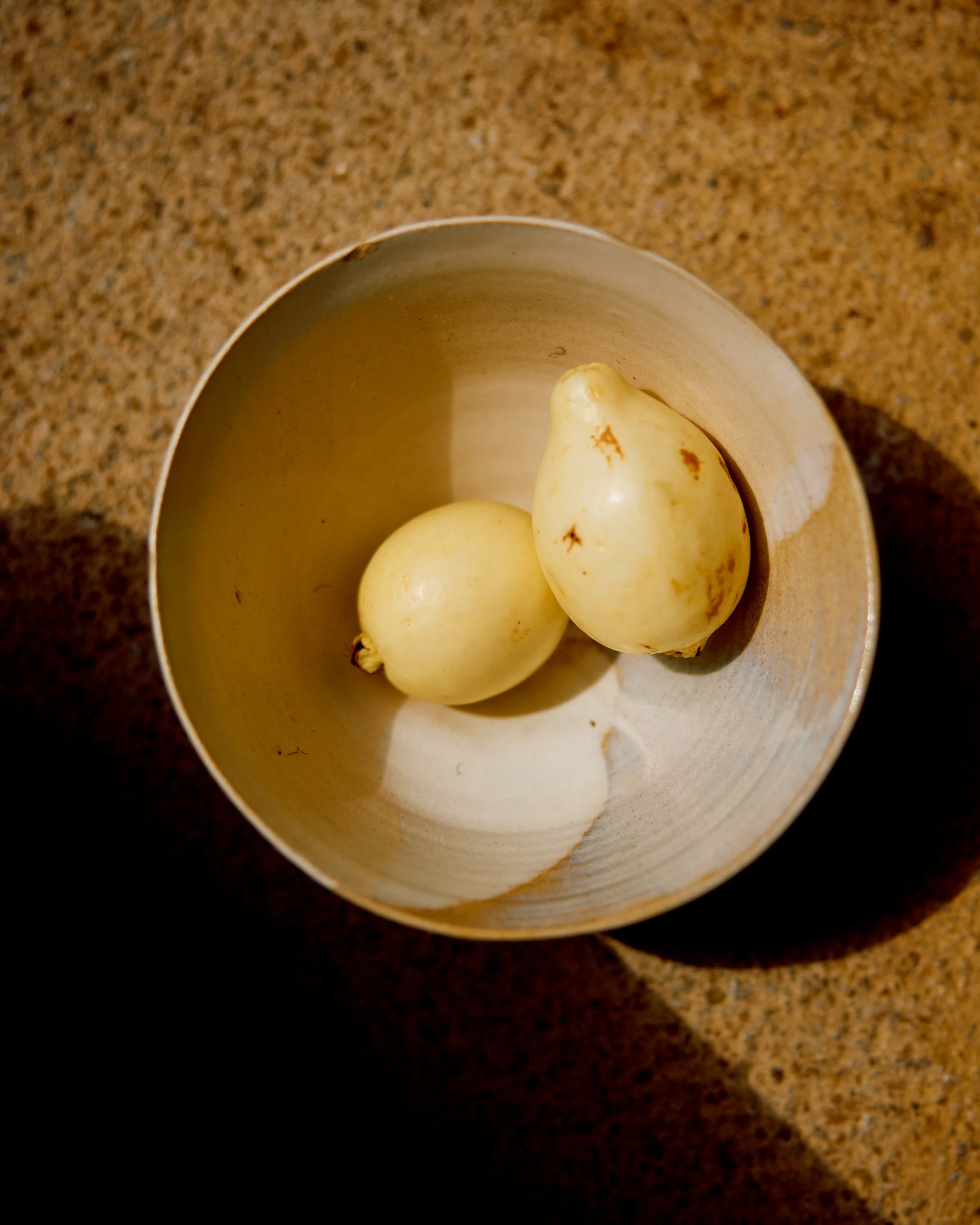 Three white onions in a beige ceramic bowl on a brown speckled countertop.