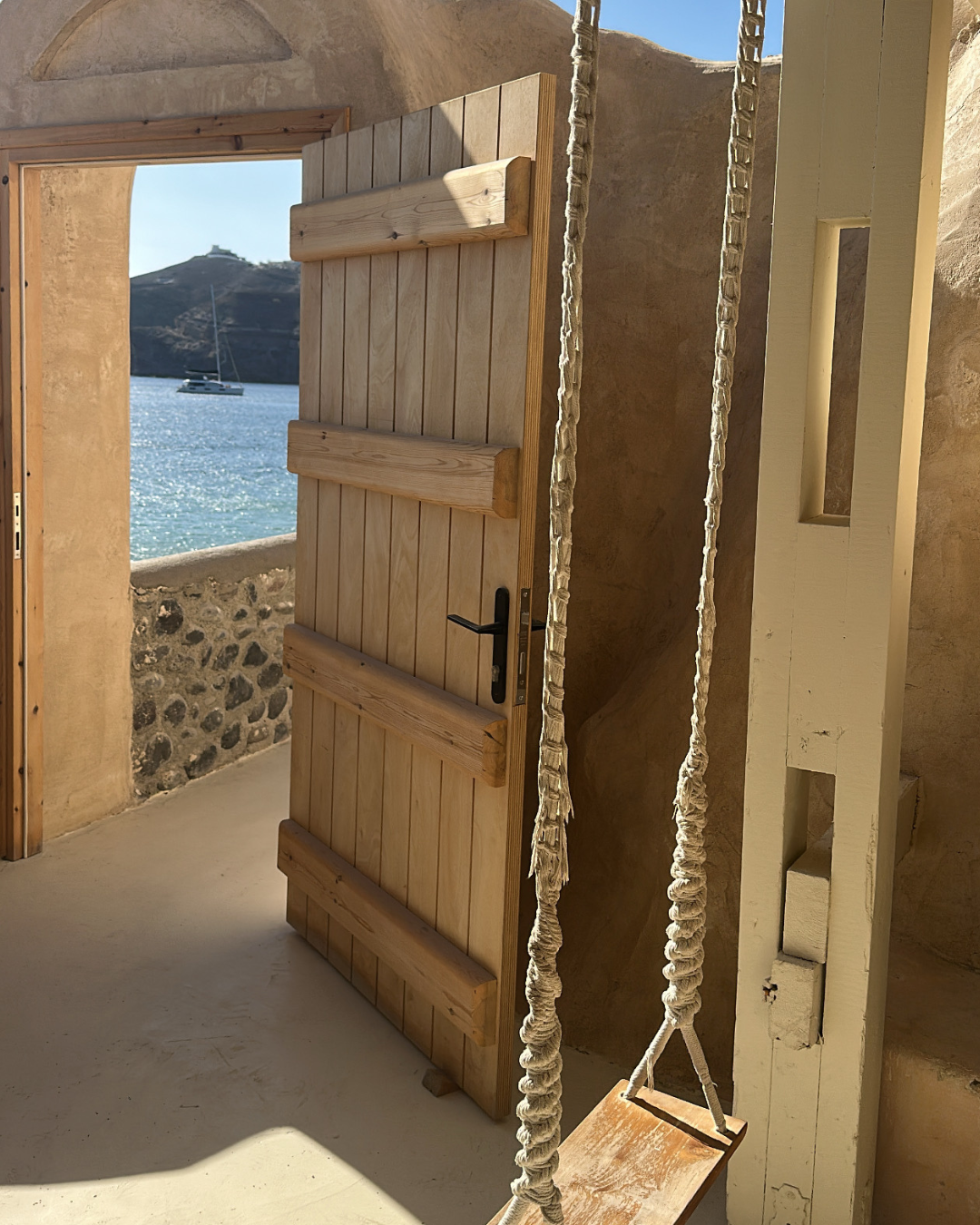 A wooden door partly open, revealing a view of the ocean with a boat and distant island.