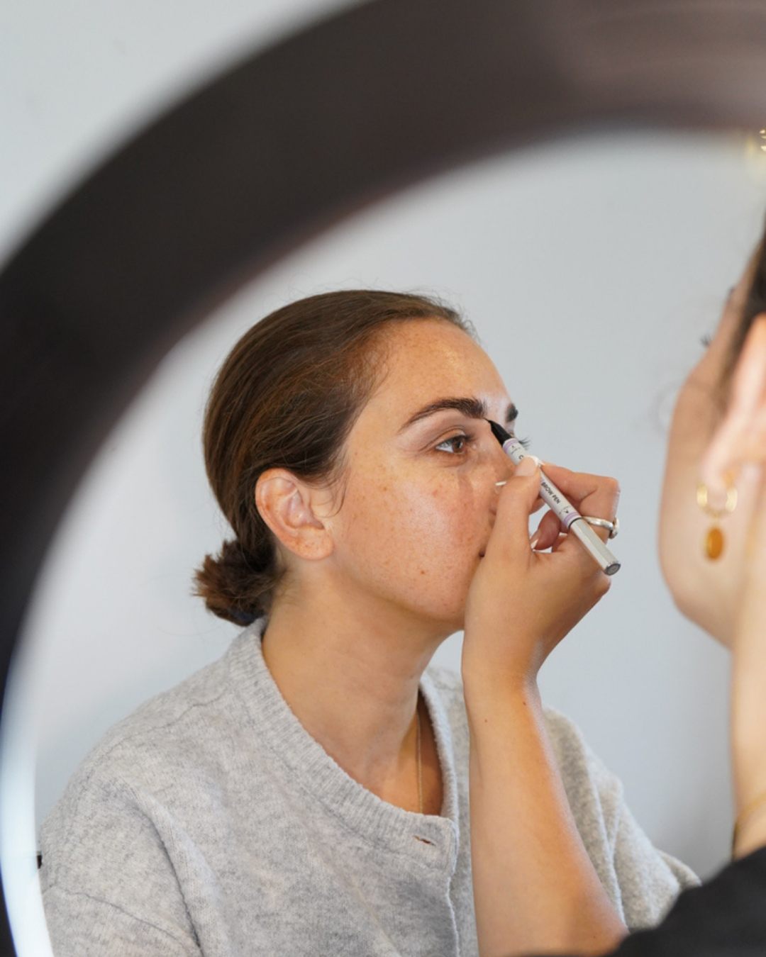 Makeup artist applying eyeliner to a woman’s eye with a pencil