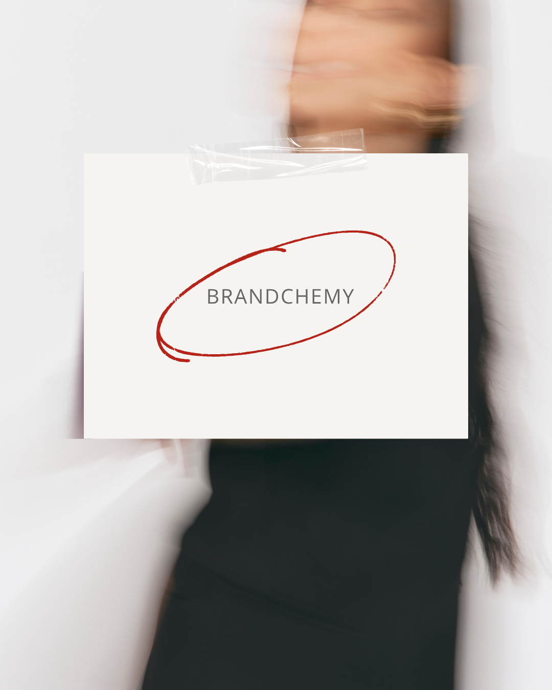 Person holding a white sign with the word 'BRANDCHEMY' surrounded by a red elliptical sketch, blurred background.
