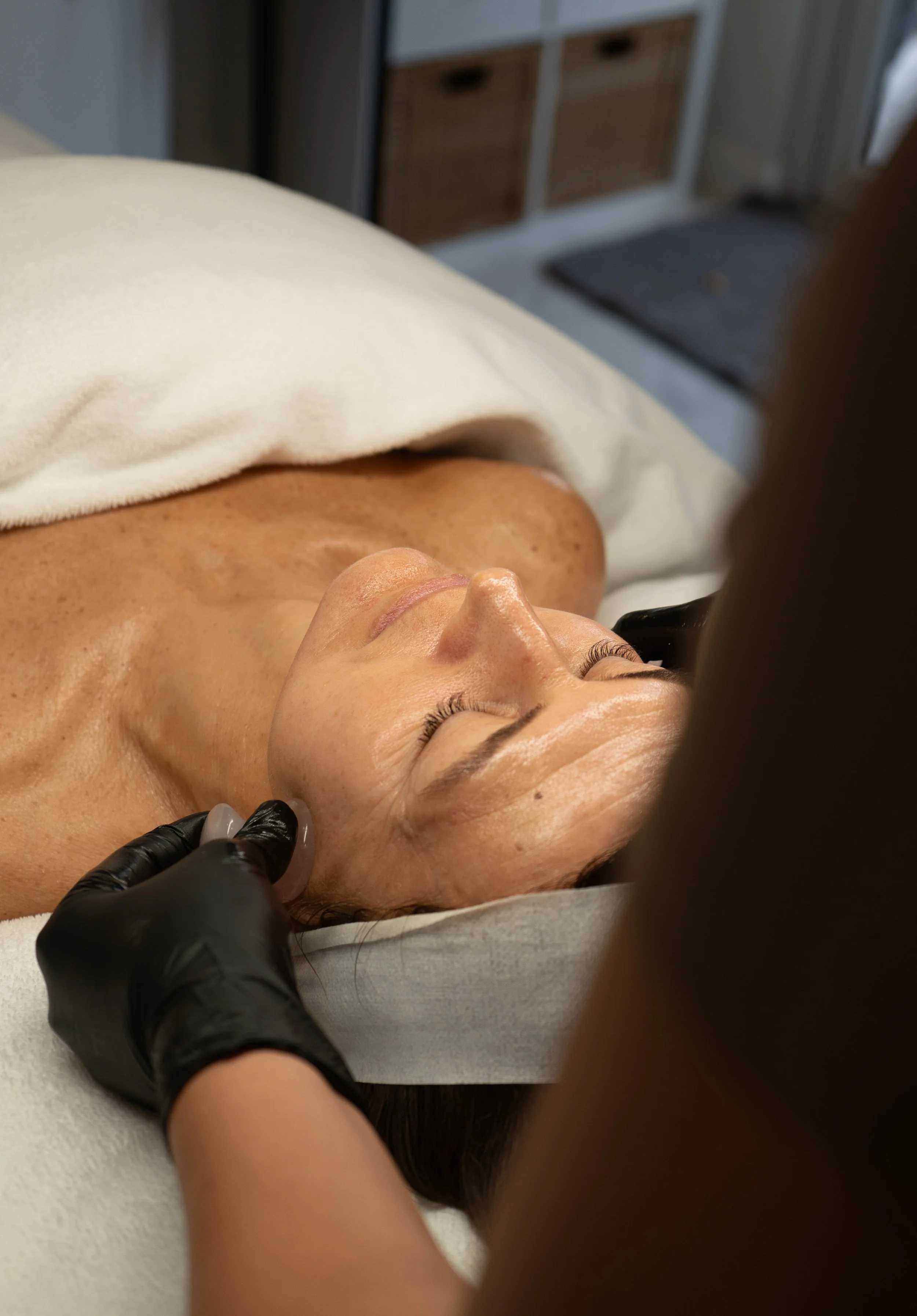 Woman receiving a facial treatment with a gloved esthetician applying a skincare device near her cheek.