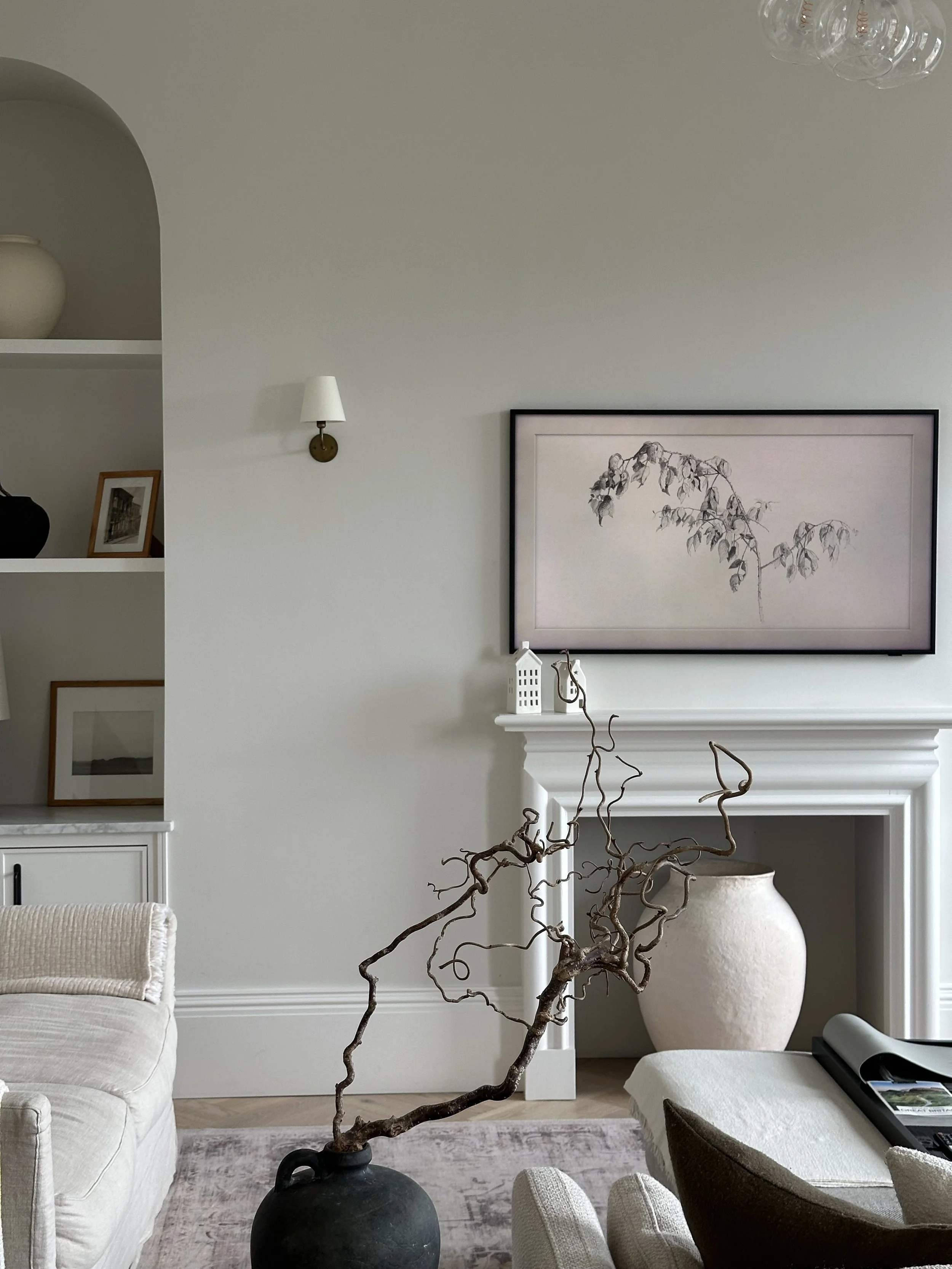 Elegant living room with a twisted branch arrangement in a black vase, white fireplace, botanical artwork, and neutral furniture.