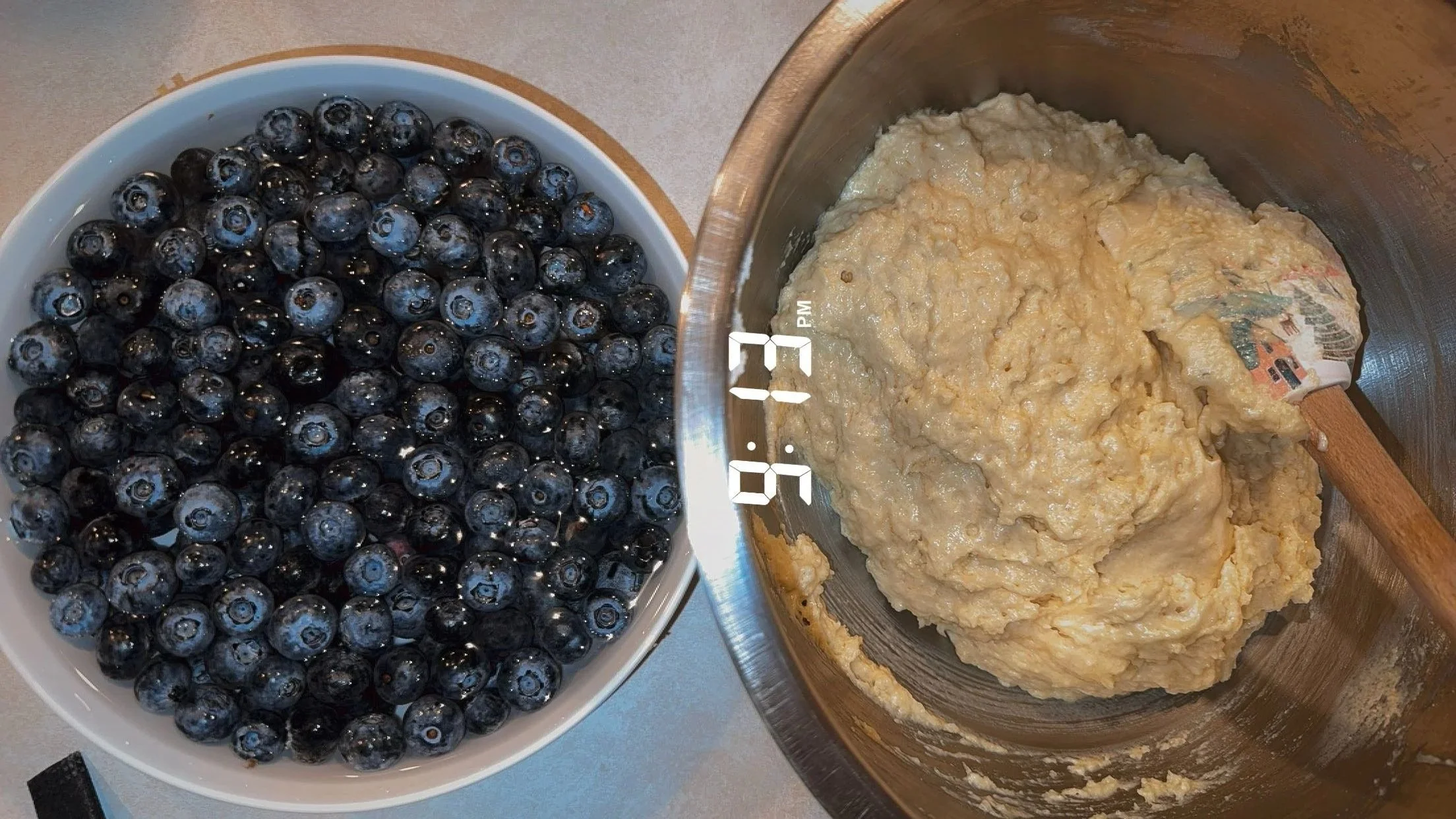A bowl of fresh blueberries next to a mixing bowl of muffin batter.