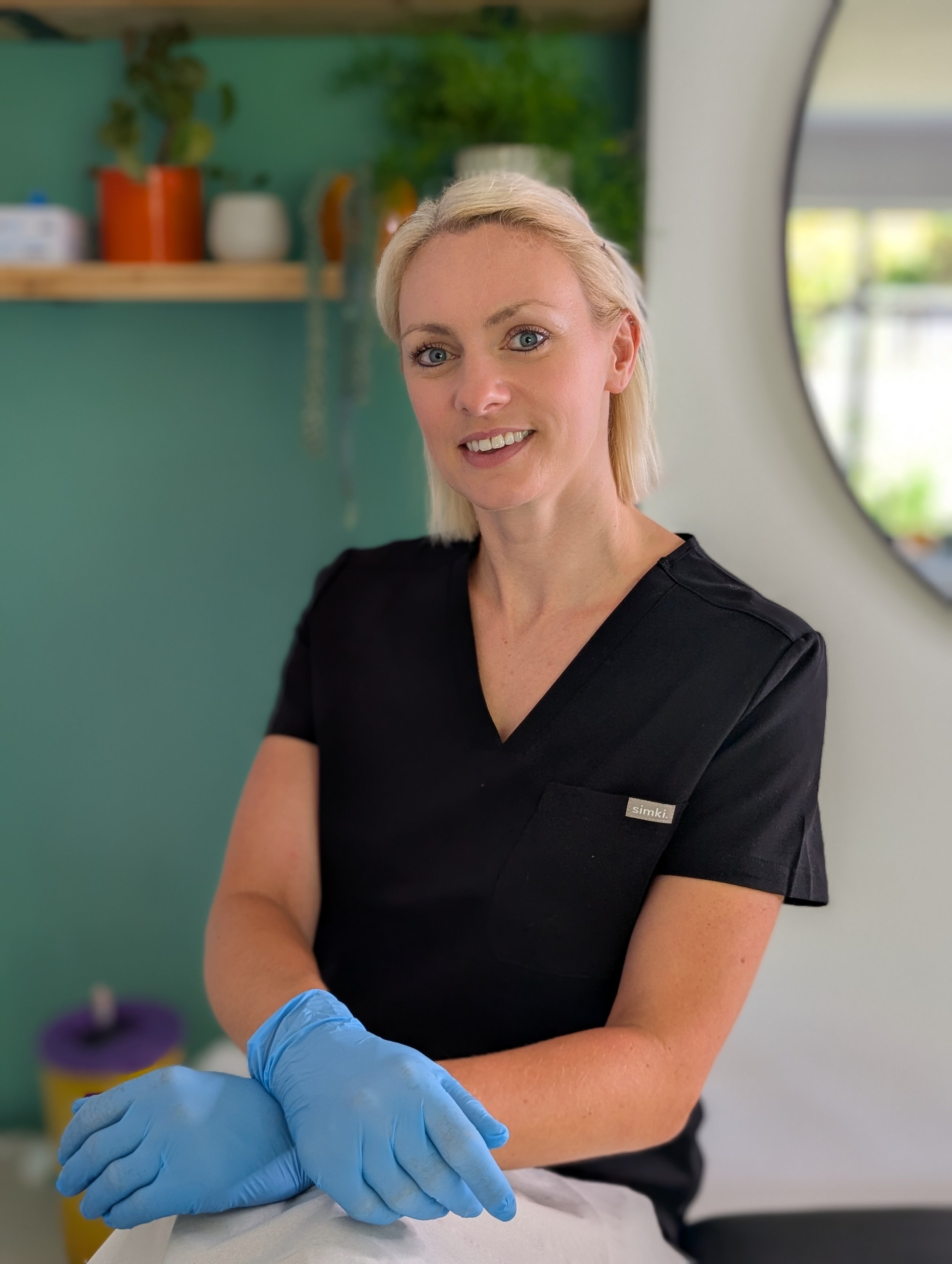 A woman in a black medical uniform wearing blue gloves and preparing to administer an injection in a clinical setting.