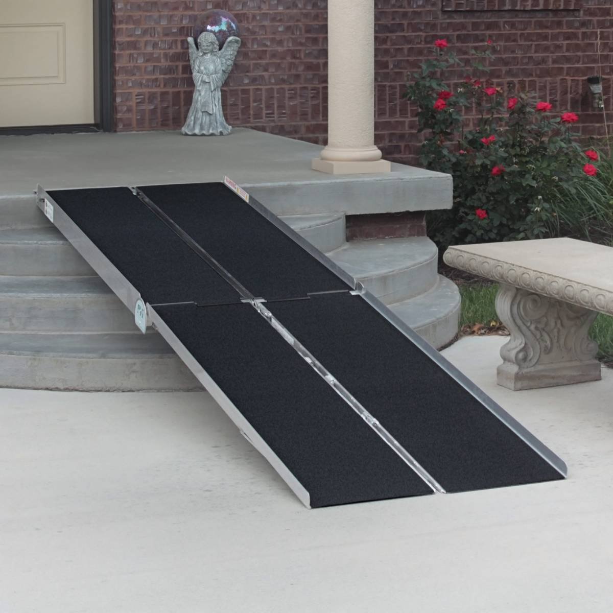 A portable wheelchair ramp leading up to a porch with steps. The porch has a decorative statue and flowers nearby.