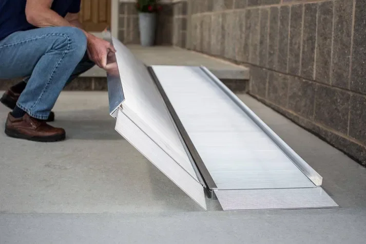 Person installing a metal or aluminum ramp on a concrete sidewalk.