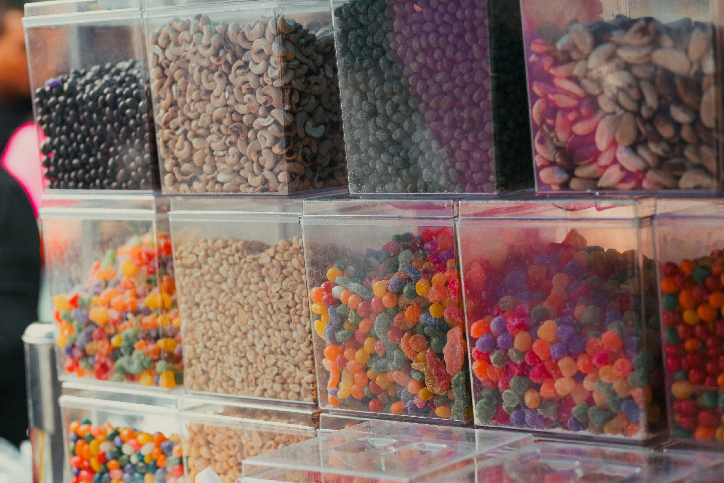 Stacked clear plastic containers filled with colorful candies and chocolates at a candy stand.