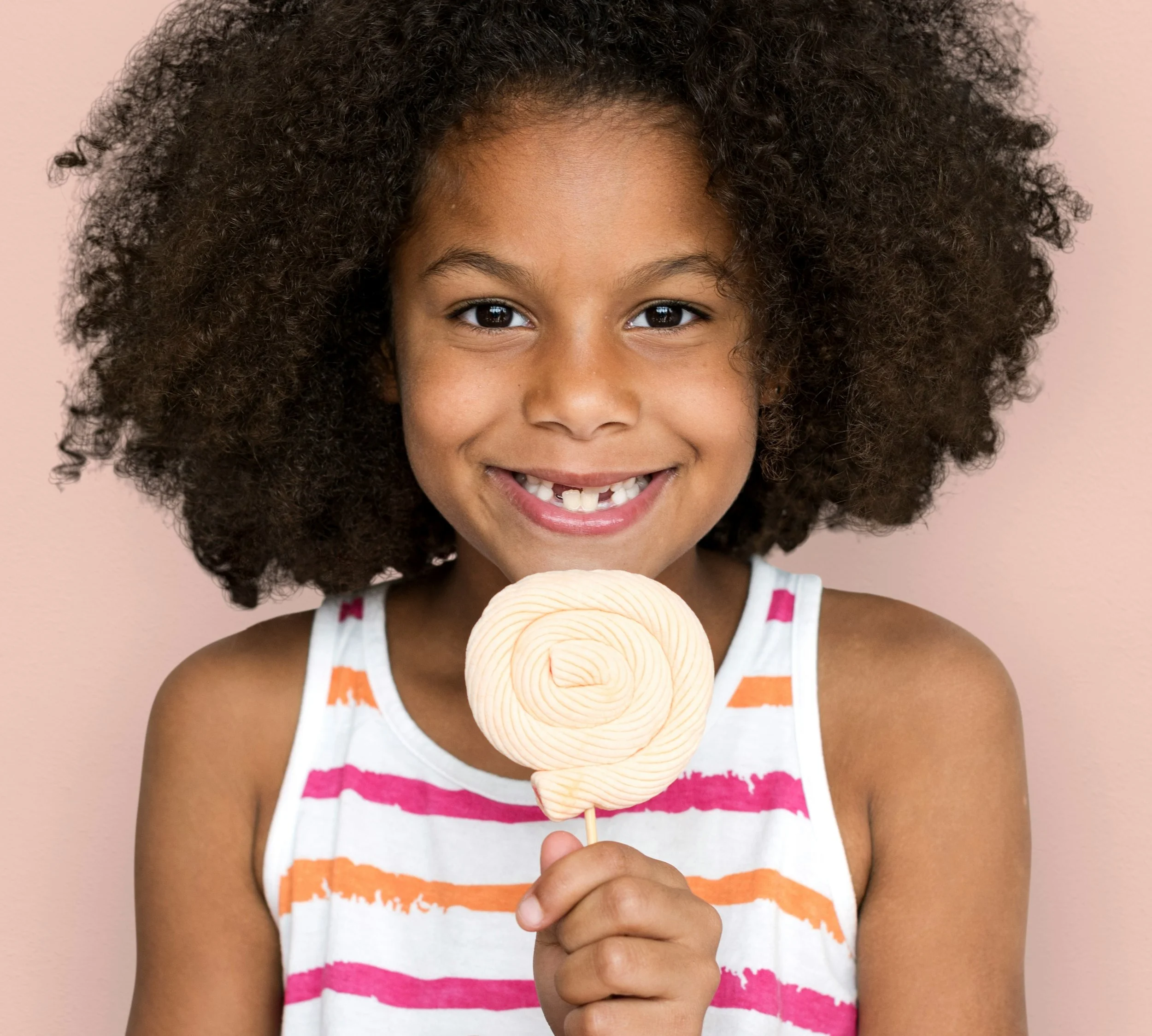 Young girl with curly hair smiling and holding a vanilla ice cream cone.