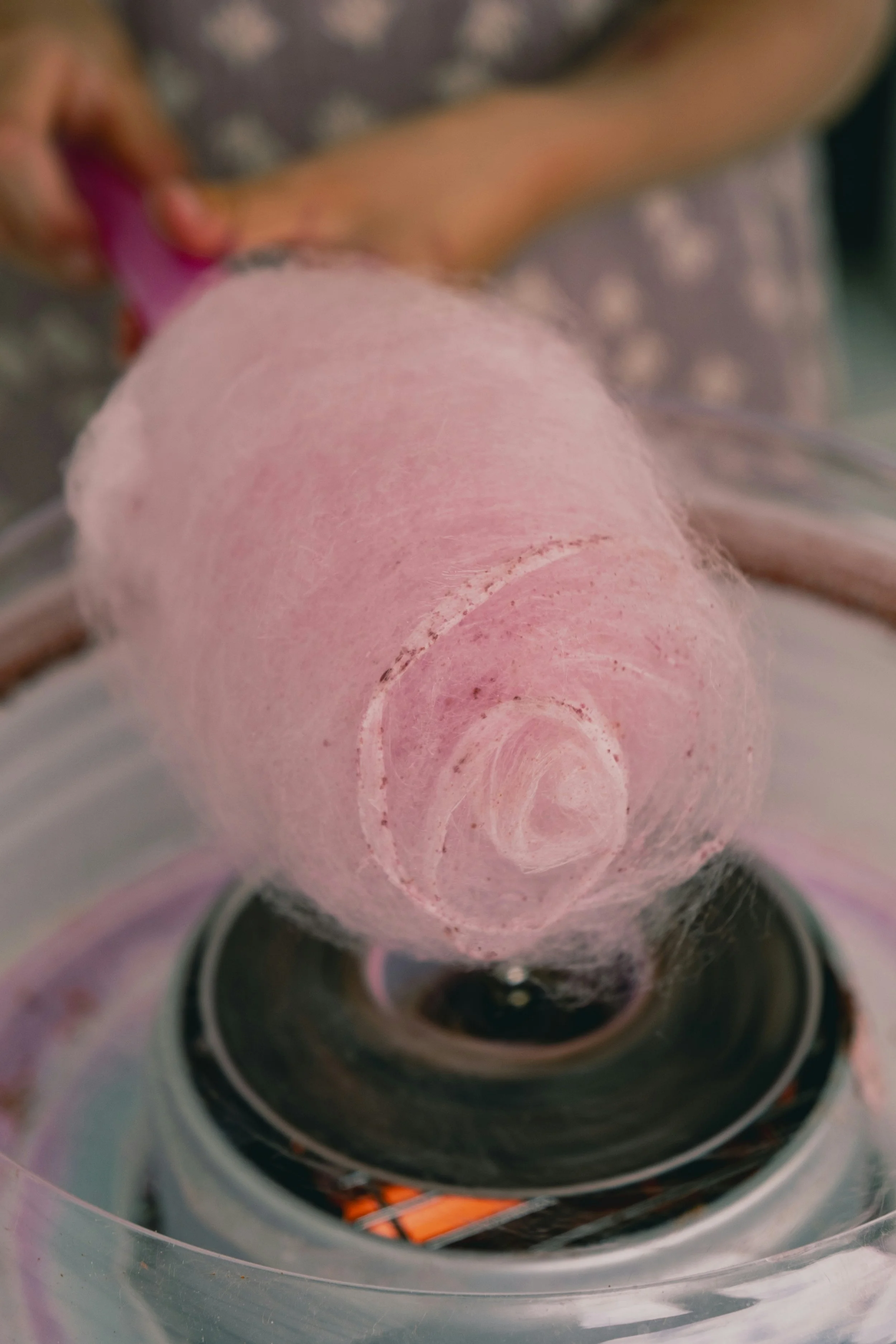Close-up of pink cotton candy held by a person's hand over an electric cotton candy machine