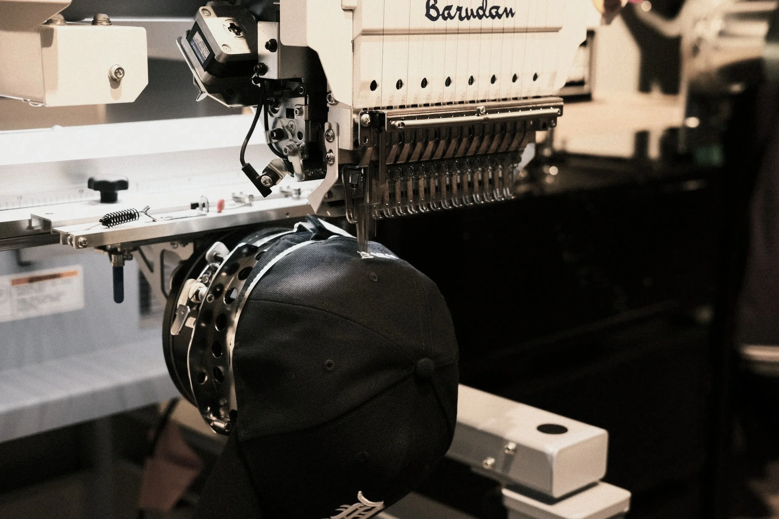 Close-up of a high-tech machine, possibly a 3D printer or industrial manufacturing equipment, with intricate mechanical parts and a dark fabric object being processed or printed.