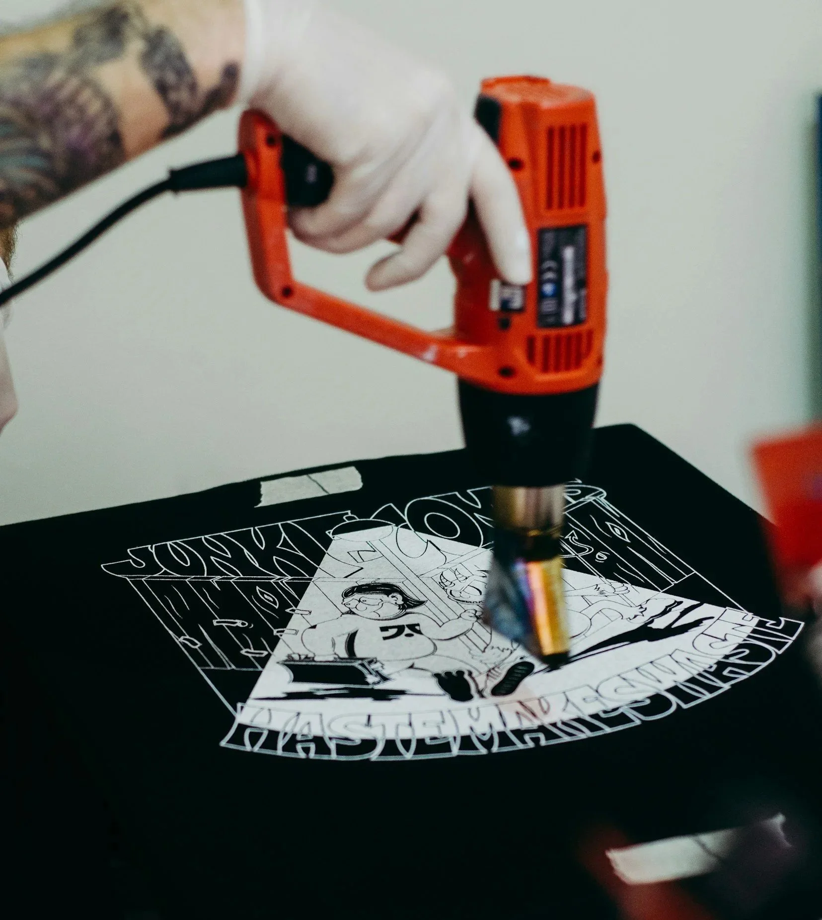 A hand wearing a glove is using a heater to adjust customization print on shirt.